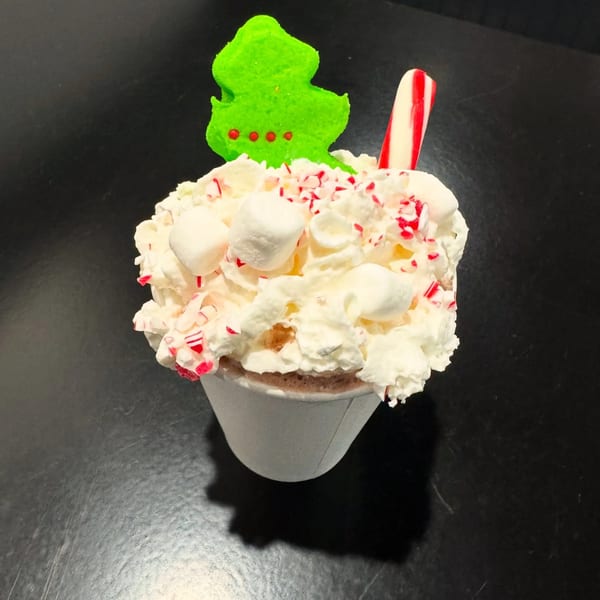 Hot chocolate with whipped cream, marshmallows, peppermint, a candy cane, and a green Christmas tree peep.