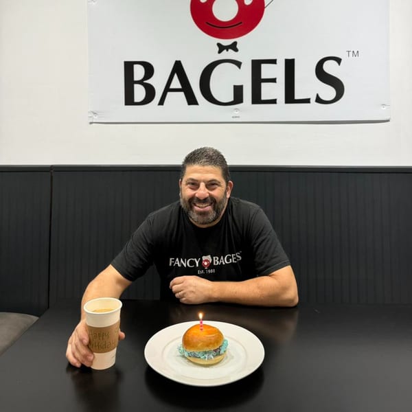 Man smiling at a table with a birthday bagel and coffee cup from Fancy Bagels.