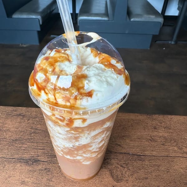A caramel frappe with whipped cream and caramel drizzle in a plastic cup with a straw.