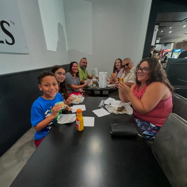 A family of six, including children and adults, happily eating bagels at a black table in Fancy Bagels.