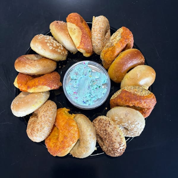 A platter of Fancy Bagels in assorted flavors surrounds a container of blue cream cheese.