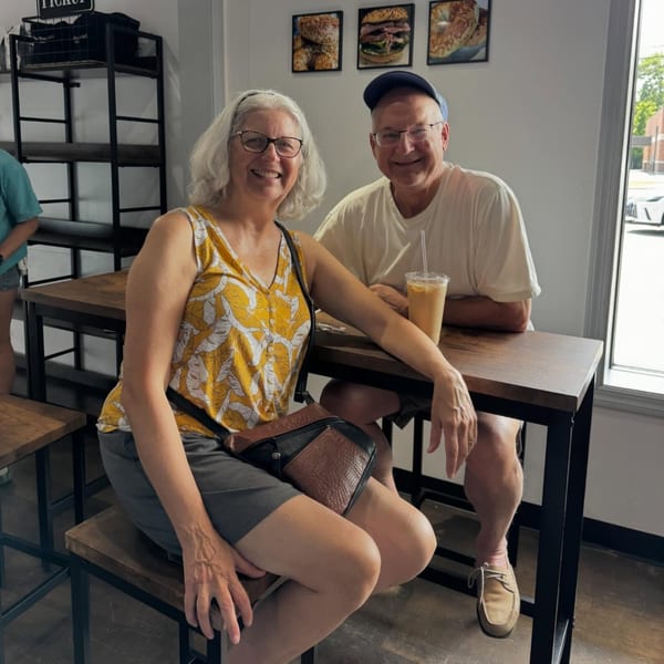 A smiling couple sits at a high-top table in Fancy Bagels, with bagel pictures on the wall.