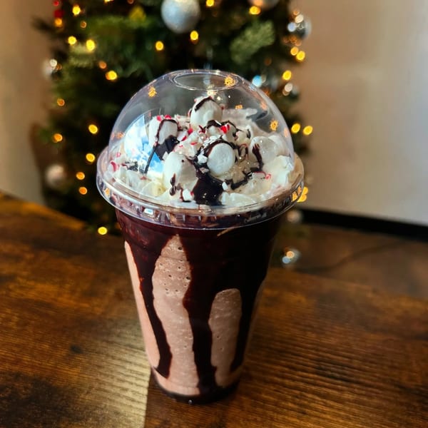Chocolate milkshake with whipped cream, marshmallows, and chocolate drizzle, in front of a Christmas tree.