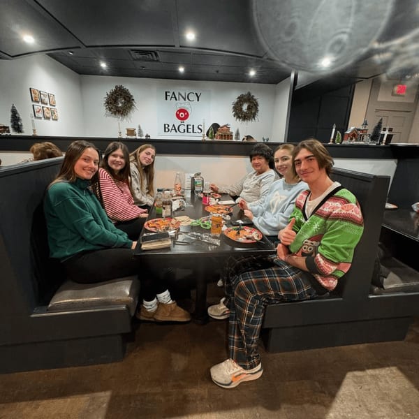 Six young people sitting at a booth table with plates of food at Fancy Bagels.